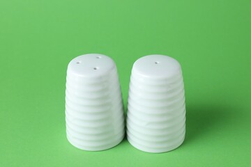 Salt and pepper shakers on green background, closeup