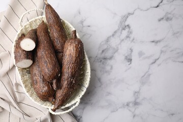 Whole and cut cassava roots in basket on white marble table, top view. Space for text