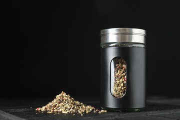 Stylish shaker with pepper on wooden board against black background, closeup. Space for text