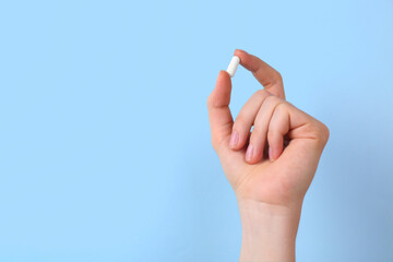 Woman holding vitamin capsule on light blue background, closeup. Space for text