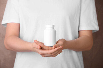 Obraz na płótnie Canvas Woman holding blank white bottle with vitamin pills against light brown background, closeup