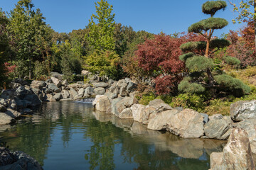 Fototapeta premium Topiary or topiary trees on shore of artificial pond with stone banks and beautiful waterfalls. Krasnodar 
