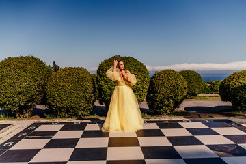 Woman yellow dress chess. A beautiful woman in a long puffy yellow dress poses on a chessboard in...