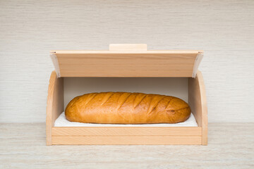 Fresh white bread in opened wooden bread box on table top at home kitchen. Closeup. Front view.