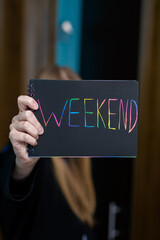 Kolorowy napis weekend na czarnej kartce w dłoniach zadowolonej kobiety  - obrazy, fototapety, plakaty