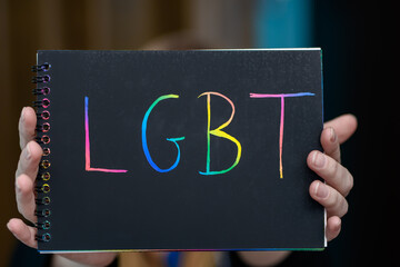 LGBT kolorowy tęczowy napis na czarnej kartce trzymany w dloni - obrazy, fototapety, plakaty
