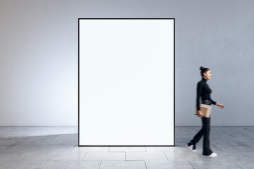 Businesswoman walking in interior with modern blank big white mock up banner frame. Museums and exhibition concept.