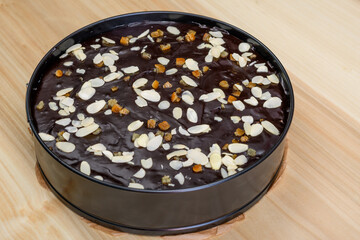 Ciasto sernik z polewą czekoladową w okrągłej formie do pieczenia, udekorwany migdałami i...