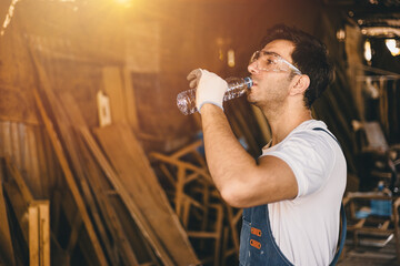Worker drinking water in an wood industrial factory. Working hydrated watering at work. Water to...