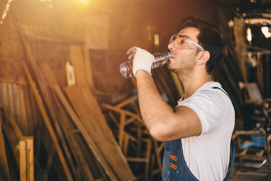 Worker drinking water in an wood industrial factory. Working hydrated watering at work. Water to the body healthcare.