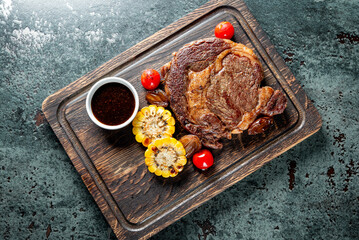 Grilled Ribeye Steak on wooden board, prime cowboy steak on dark background
