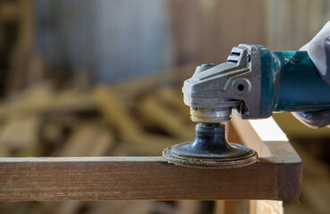 A person works with a power tool, sending sawdust flying as they cut or shape a piece of wood.