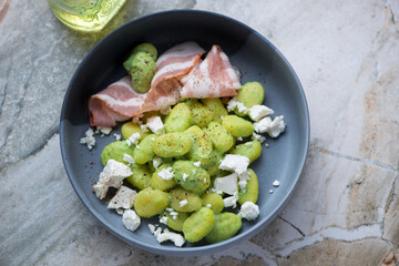Bowl of italian gnocchi with green pea sauce and bacon, horizontal shot on a grey granite background, elevated view