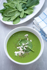 White bowl with spinach cream-soup on a light-grey granite background, vertical shot, elevated view