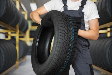 Car mechanic is holding winter tire in hands.