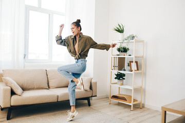 Joyful Woman Jumping and Dancing in a Home Apartment, Enjoying Music and Relaxation on Sofa