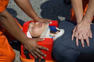 A man in head immobilizer tool lying on stretcher long spinal board with safety belt get CPR from...