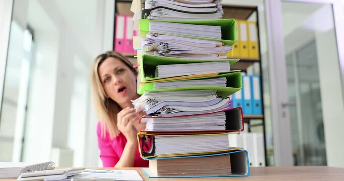 Shocked woman looks at stack of folders on desk to work with