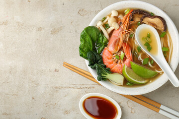 Delicious ramen with shrimps and mushrooms in bowl served on light textured table, flat lay and...