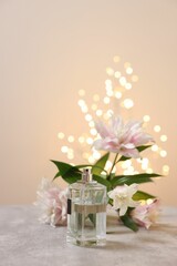 Bottle of perfume and beautiful lily flowers on table against beige background with blurred lights, space for text