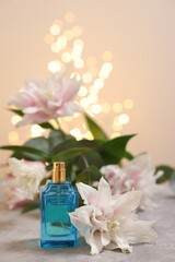 Bottle of perfume and beautiful lily flowers on table against beige background with blurred lights,...