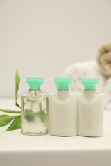 Mini bottles of cosmetic products and green branch on white table