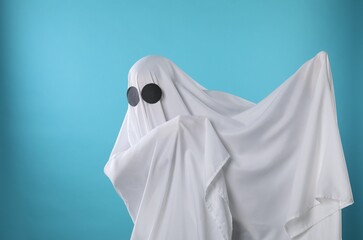 Creepy ghost. Person covered with white sheet on light blue background, space for text
