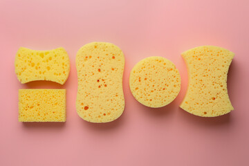 New yellow sponges of different shapes on pink background, flat lay