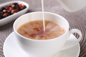 Pouring milk into cup with aromatic tea at table, closeup - Powered by Adobe