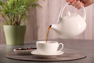 Woman pouring tea into cup at grey table, closeup