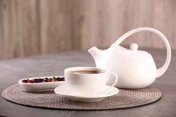 Aromatic tea in cup, saucer, teapot and dry flower petals on grey table