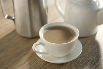 Aromatic tea with milk in cup, teapot and pitcher on wooden table, closeup