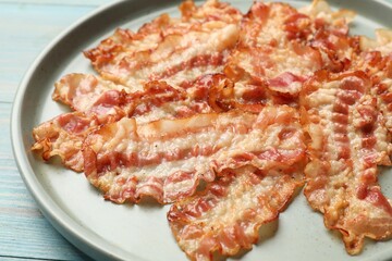 Delicious fried bacon slices on blue wooden table, closeup