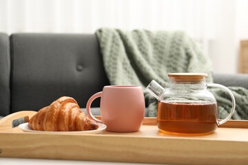 Aromatic tea in teapot, cup and tasty croissant on table indoors