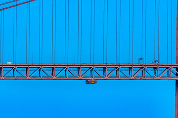 Part of the 25 de Abril suspension bridge with red steel cables that support the structure where...
