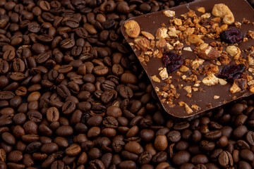 A bar of craft chocolate with various nuts, berries and dried fruits. Coffee beans. Food brown background