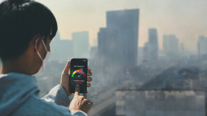 Asian man wearing the N95 using a smartphone app showing PM 2.5 dust in the capital that exceeds...