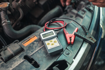 A digital battery tester connected to a car battery, checking for performance and charge level..