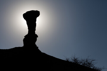 Backlit silhouette of a geological formation against the background of a blue sky. This geological...