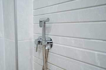 Chrome bidet sprayer with a long hose mounted on white ceramic tiles in the bathroom