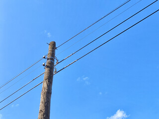 Old power line pole against blue sky in sunny day