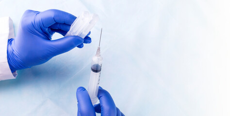 Medical gloved hands holding syringe with a bead of liquid emerging testing the function of the...