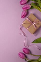 Beautiful gift box with ribbon and pink tulips on light purple background. Flat lay, top view. Space for text. 