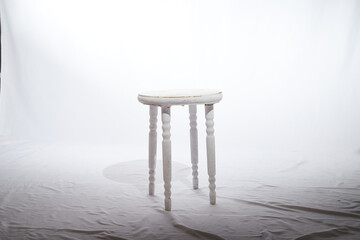 Solitary Wooden Stool in a White Minimalist Setting. Lone, white-painted wooden stool stands...