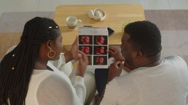 High angle back view of black couple talking about unborn baby looking at ultrasound image at homeHigh angle back view of black couple talking about unborn baby looking at ultrasound image at home