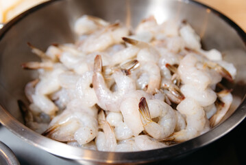 Raw Shrimp Piled in Stainless Steel Bowl. A pile of raw, peeled shrimp in a stainless steel bowl, prepared for cooking, with a focus on fresh seafood ingredients.