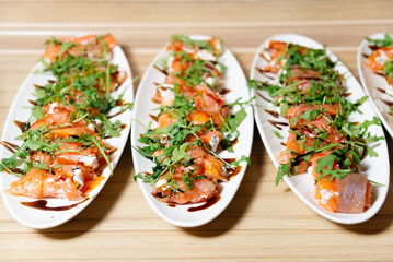 Smoked Salmon Appetizers with Arugula and Balsamic. White platters filled with smoked salmon rolls topped with fresh arugula, cream cheese, and drizzled with balsamic glaze, ready for serving.