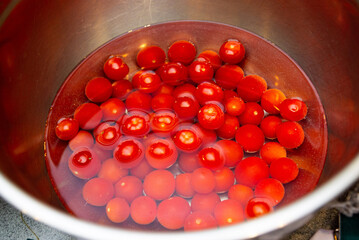 Cherry Tomatoes Washing in Water in Metal Bowl. Bright red cherry tomatoes floating in water in a stainless steel bowl, being washed before eating or cooking.