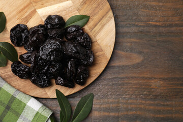 Tasty dried prunes and green leaves on wooden table, top view. Space for text