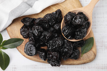 Spoon with tasty dried prunes and green leaves on light wooden table, top view
